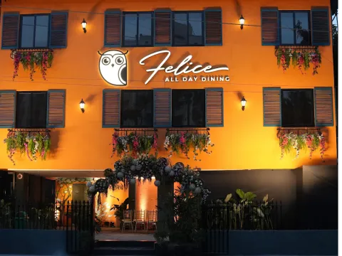 The orange facade of Felice All Day Dining at dusk, with its owl sign lit