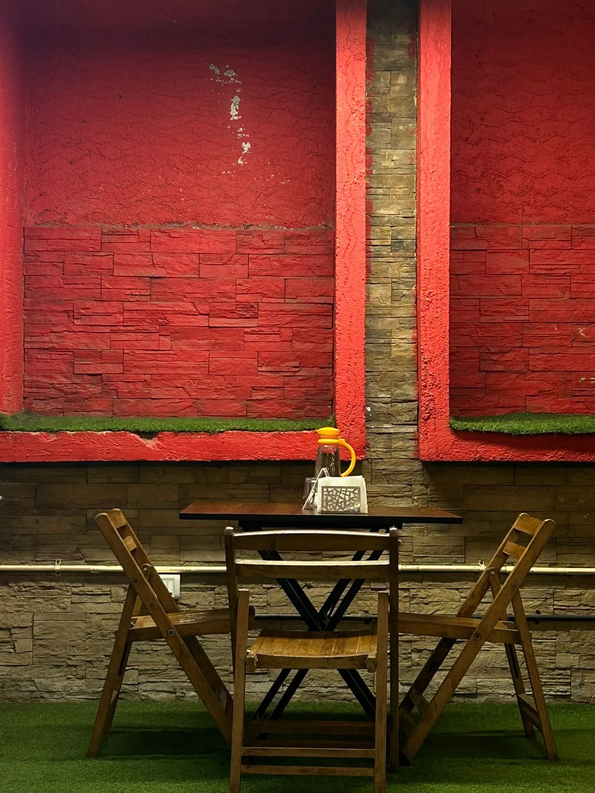 A single wooden table against the red wall of the old backyard